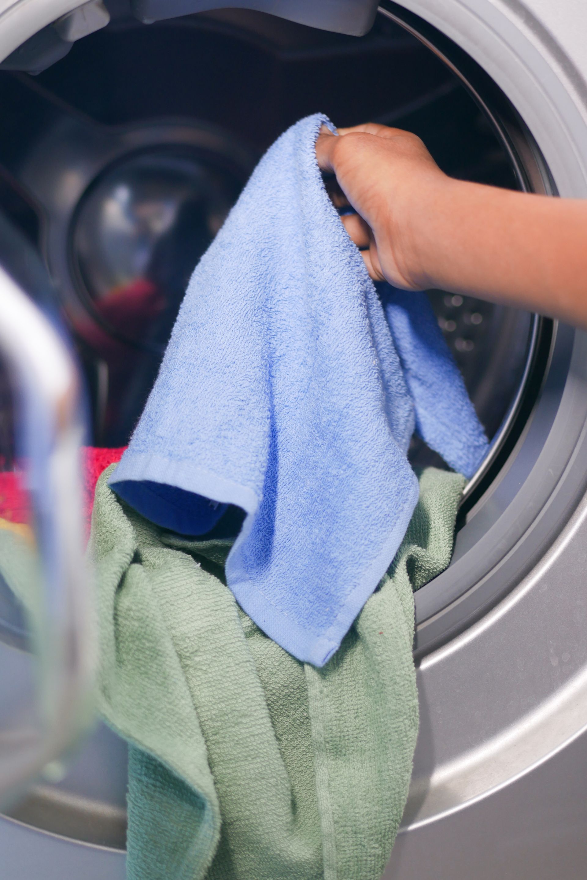 Hands holding blue and green microfiber cloths beside an open washing machine drum Hands holding blue and green microfiber cloths beside an open washing machine drum