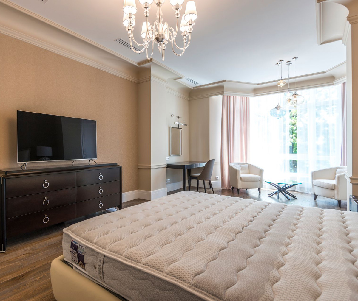 Upscale bedroom with a chandelier, dresser, TV, and a made bed with a footboard bench Upscale bedroom with a chandelier, dresser, TV, and a made bed with a footboard bench