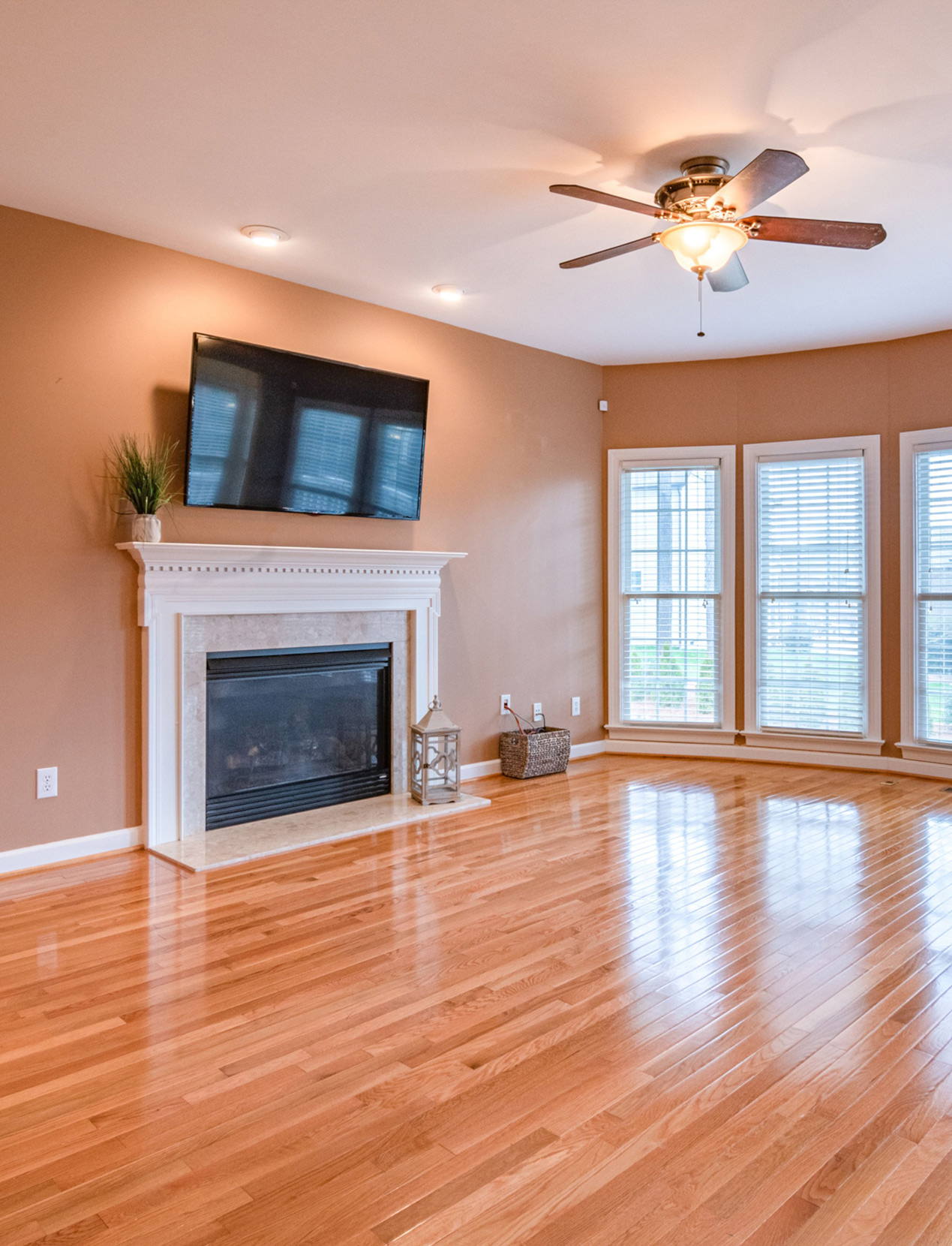 Living room with a fireplace, wall-mounted TV, and glossy hardwood flooring