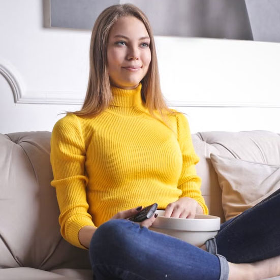 Kate, a Heaven's Best customer, smiling while seated on a couch in a yellow sweater