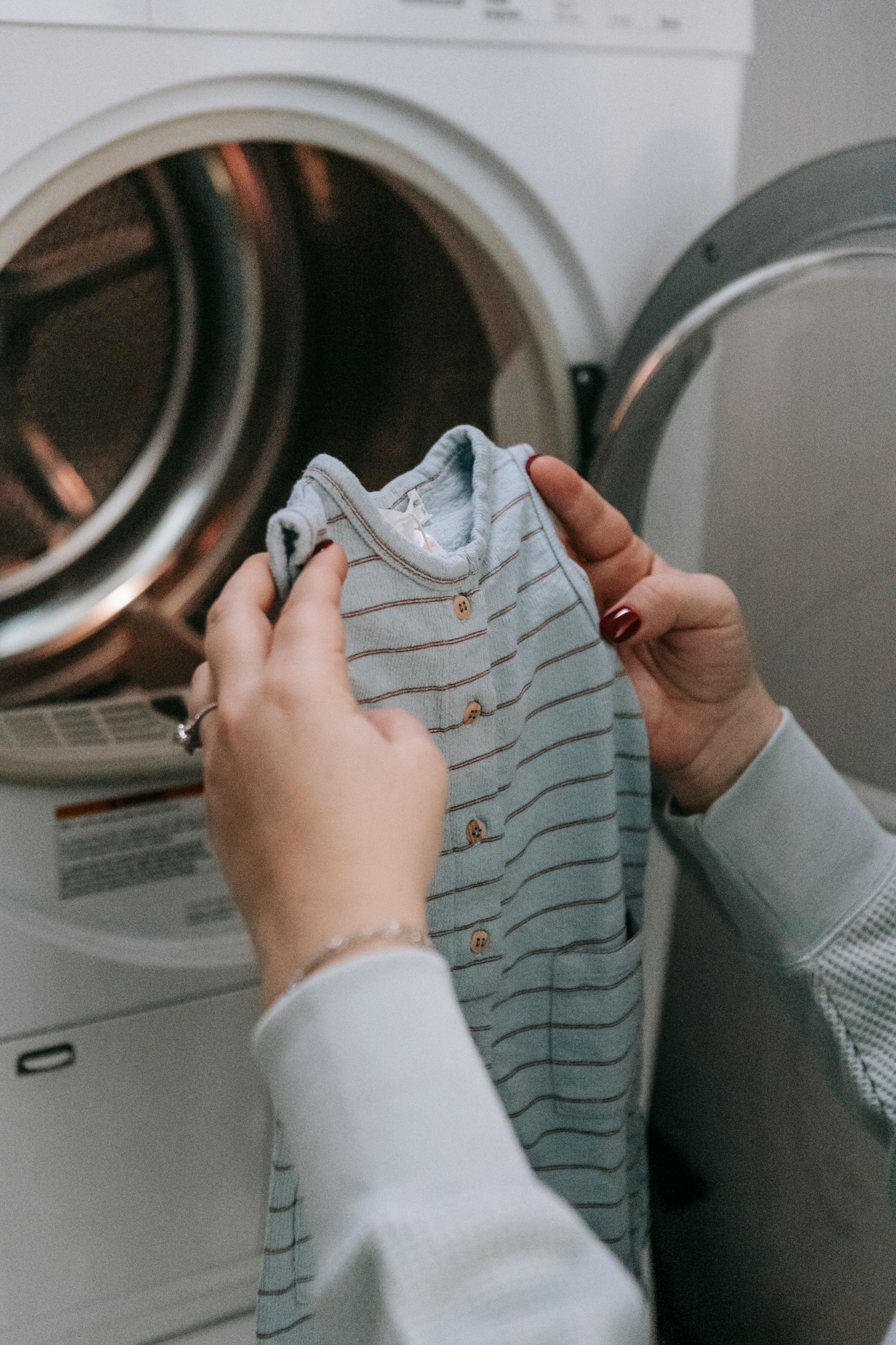 Woman folding a striped garment in front of a washer and dryer at home Woman folding a striped garment in front of a washer and dryer at home