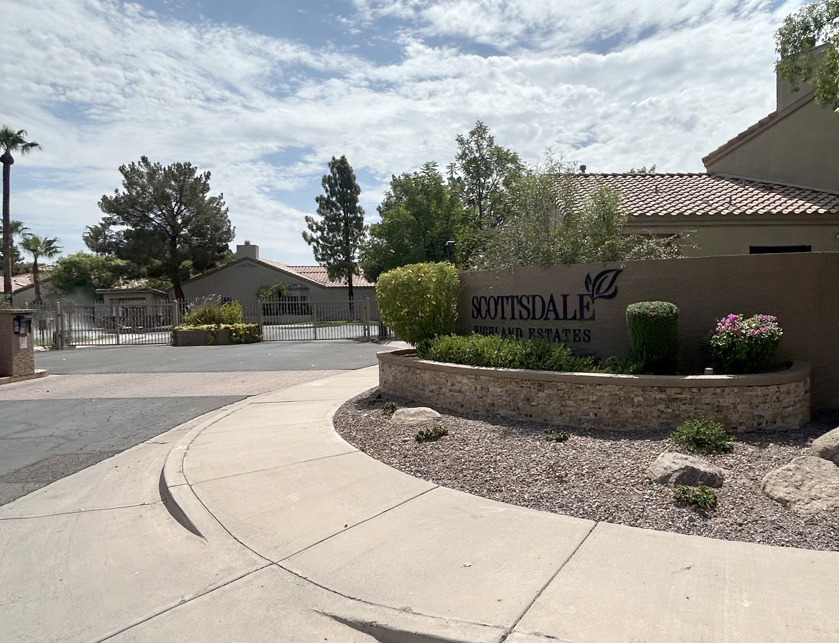 Gated Scottsdale community entrance with a monument sign, stone planter, and flowering shrubs