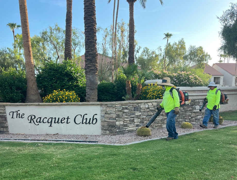Two TerraPro crew members using backpack blowers at The Racquet Club community entrance sign
