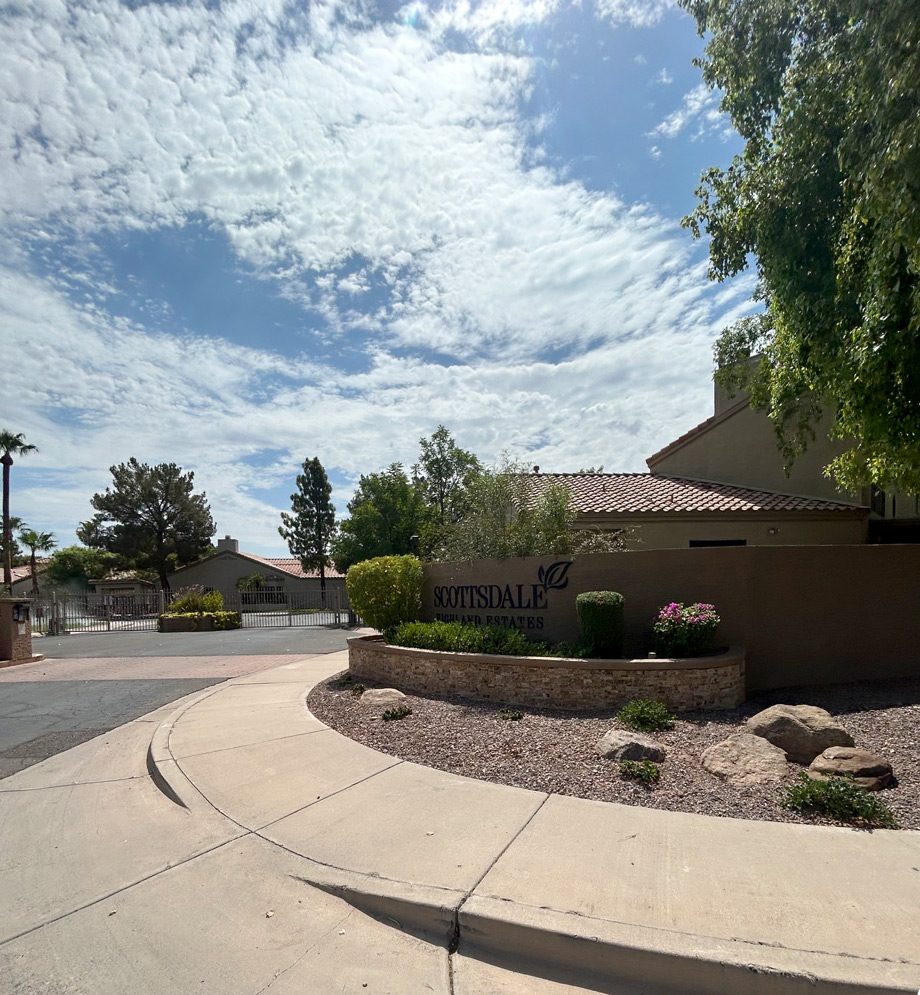 Gated Scottsdale community entrance monument beside a curving drive under a wide cloudy sky