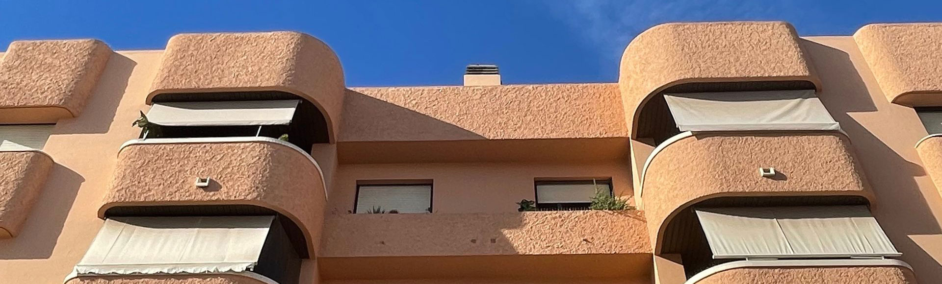 Stucco apartment building exterior with tan awnings shading the second-floor balconies Stucco apartment building exterior with tan awnings shading the second-floor balconies