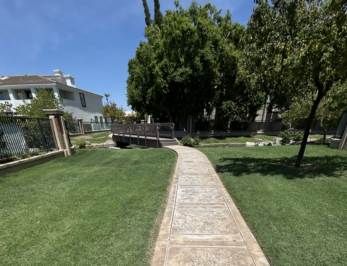 Concrete walkway through a mown HOA lawn, shaded by mature trees beside two-story homes Concrete walkway through a mown HOA lawn, shaded by mature trees beside two-story homes
