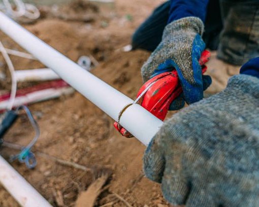 Gloved hands repairing a PVC irrigation pipe fitting