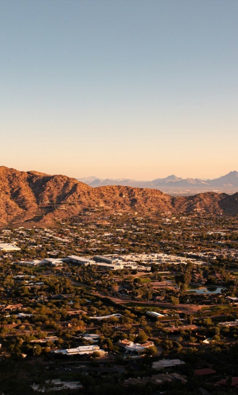 Phoenix neighborhood at sunset with desert mountain ridges rising behind the rooftops