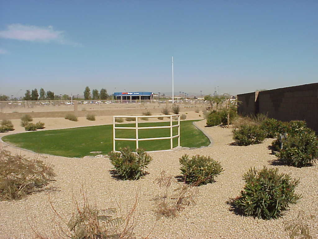 Open desert retention basin with a white shade ramada and low shrubs behind a block wall Open desert retention basin with a white shade ramada and low shrubs behind a block wall