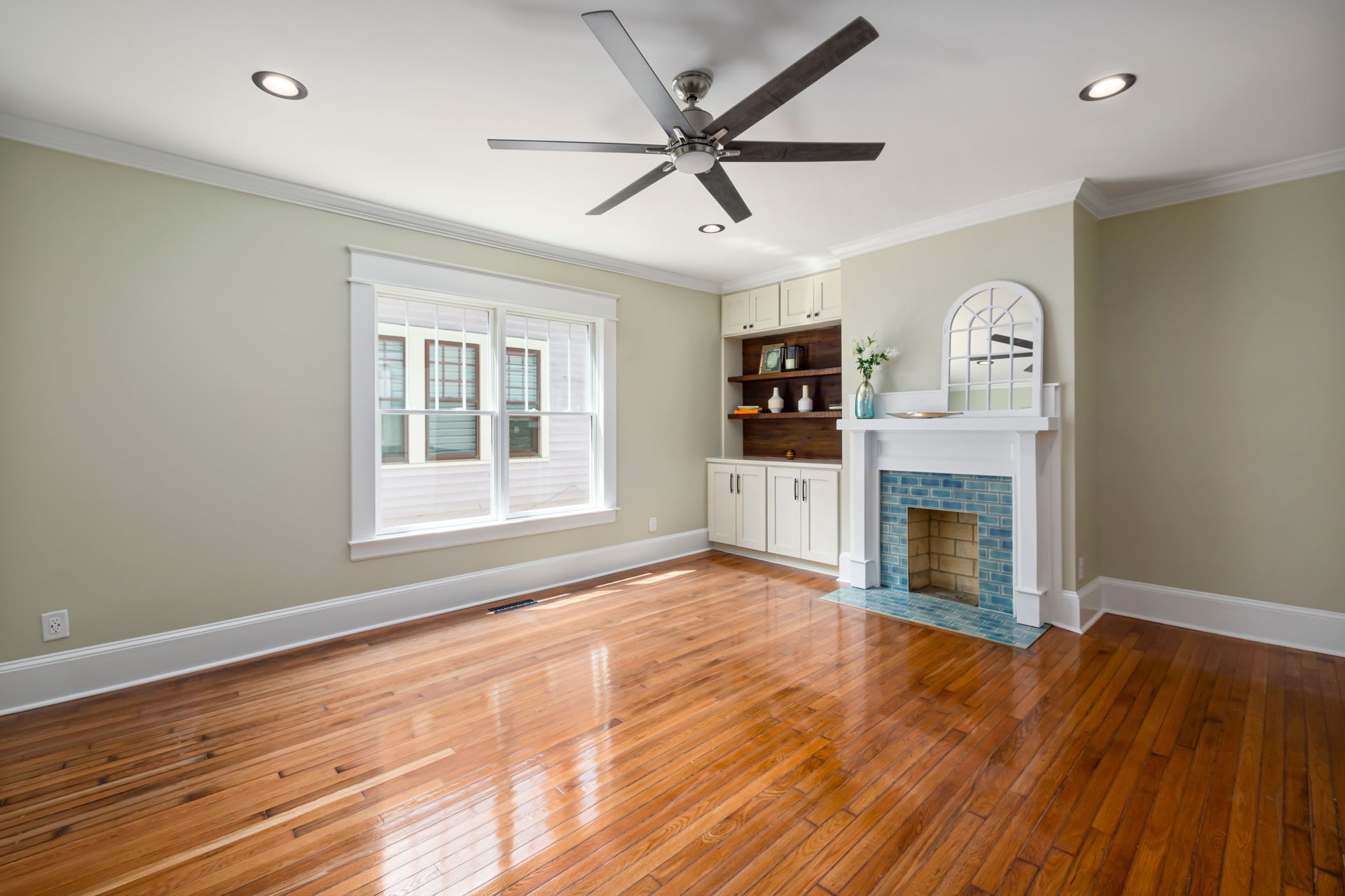 Empty room with polished hardwood flooring and a fireplace with a blue-tiled surround