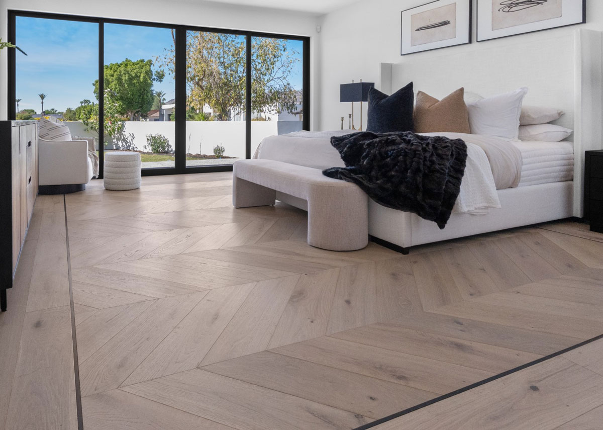 Bright bedroom with chevron-pattern white oak flooring and floor-to-ceiling windows opening to a patio Bright bedroom with chevron-pattern white oak flooring and floor-to-ceiling windows opening to a patio