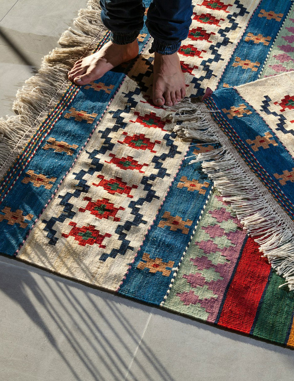 Bare feet resting on a freshly cleaned striped kilim rug with fringed edges on tile flooring