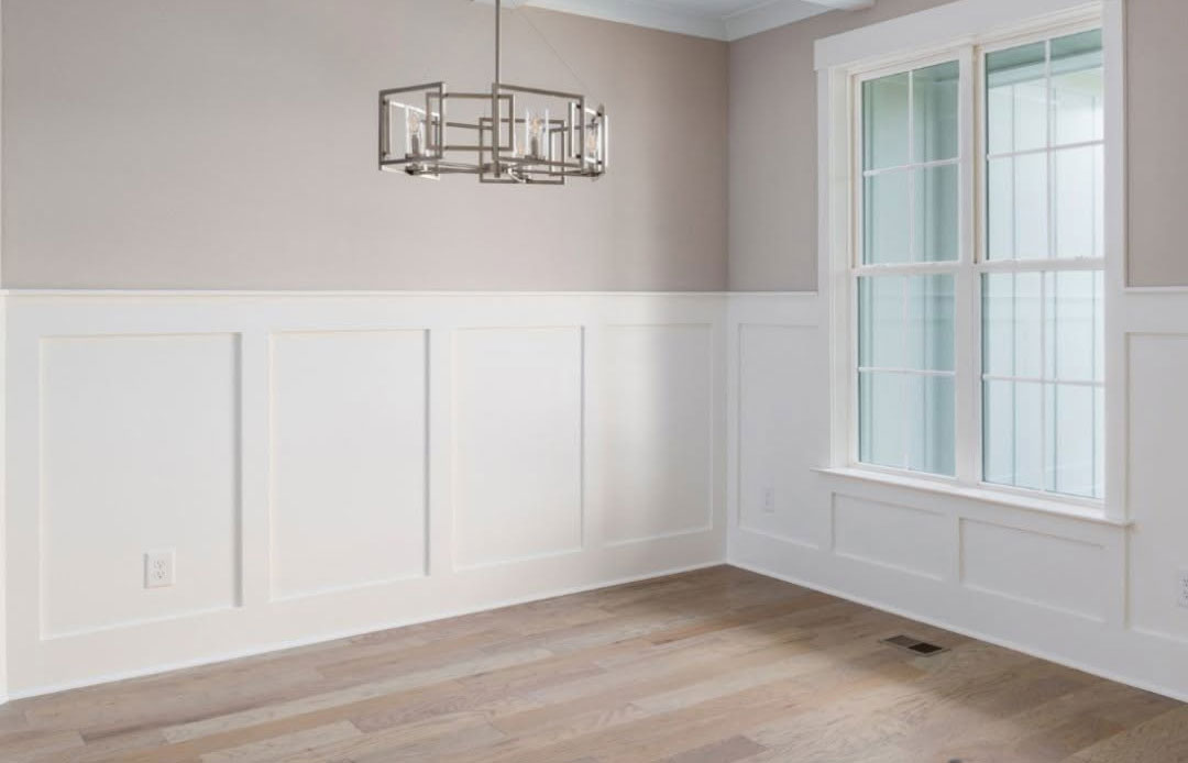 Empty dining room with white wainscoting, a black chandelier and clean light-wood flooring