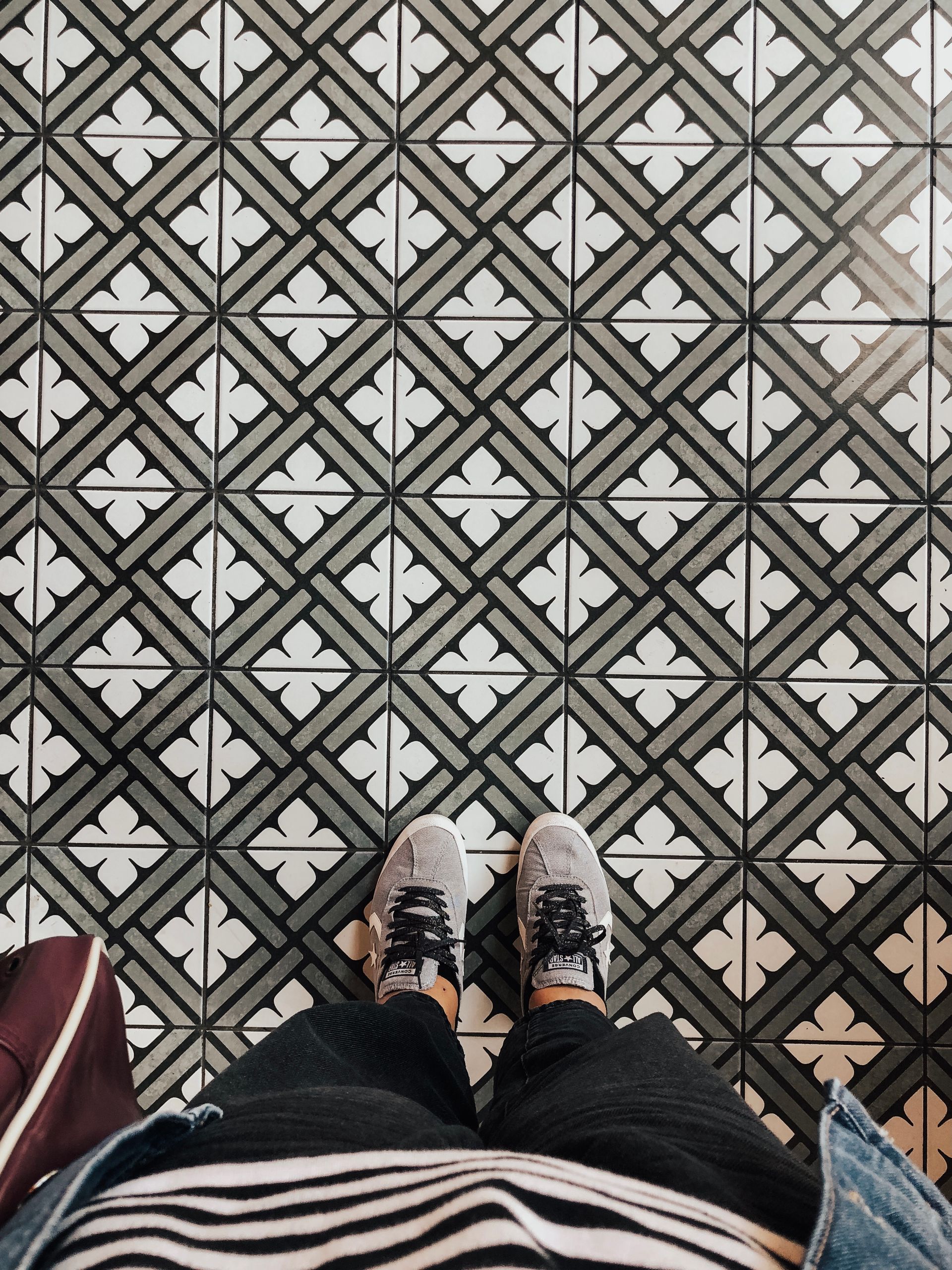 Overhead view of sneakers standing on a black-and-white patterned encaustic tile floor