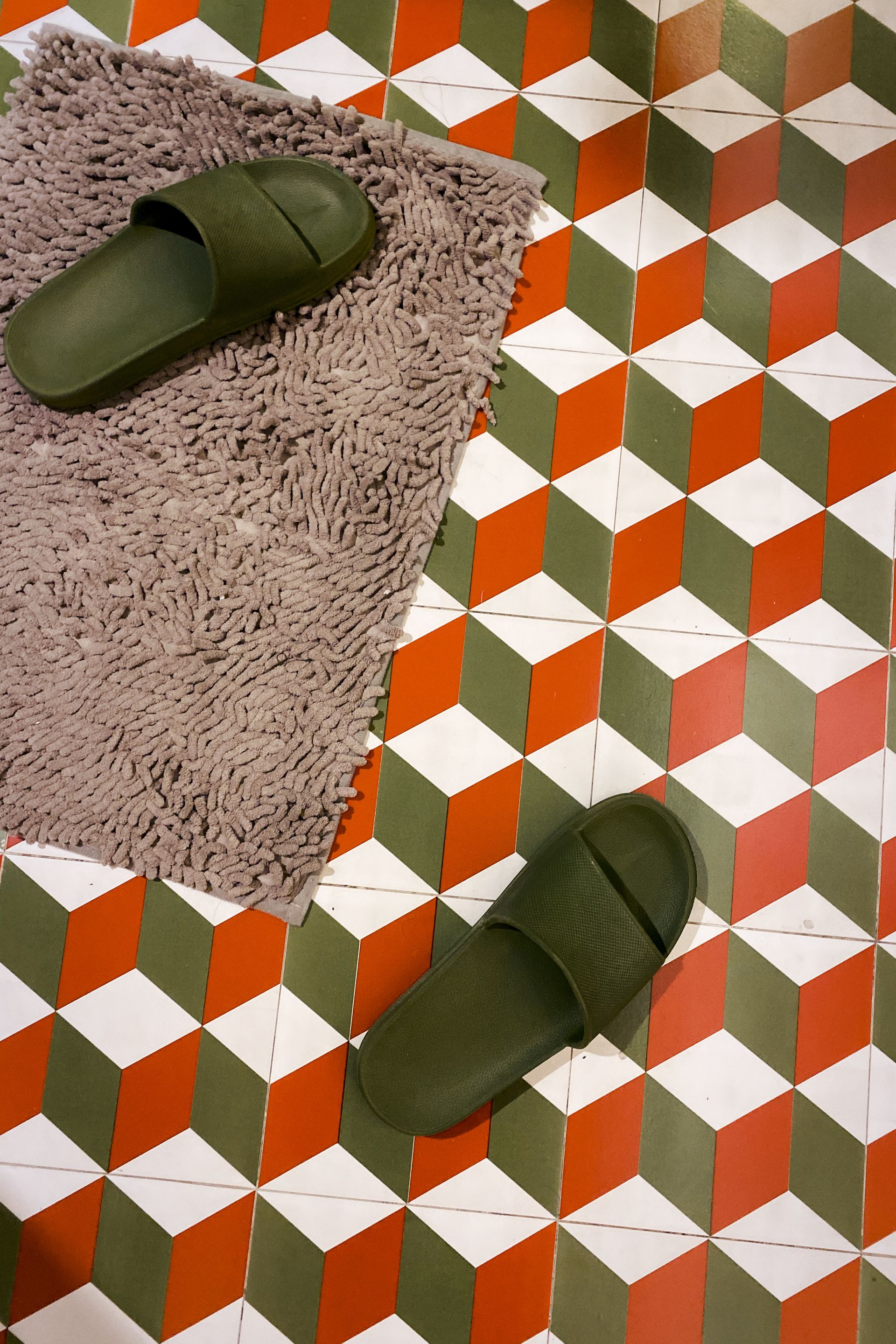 Green slippers on a pink shag bath mat beside a bold orange and green geometric tile floor