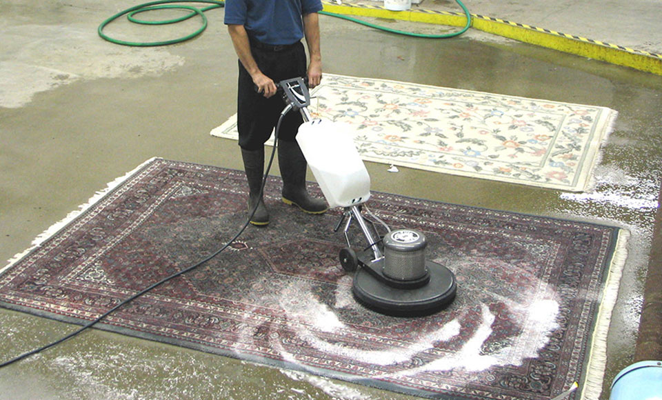 Technician running a rotary scrubber over a foamy oriental rug on the plant wash floor
