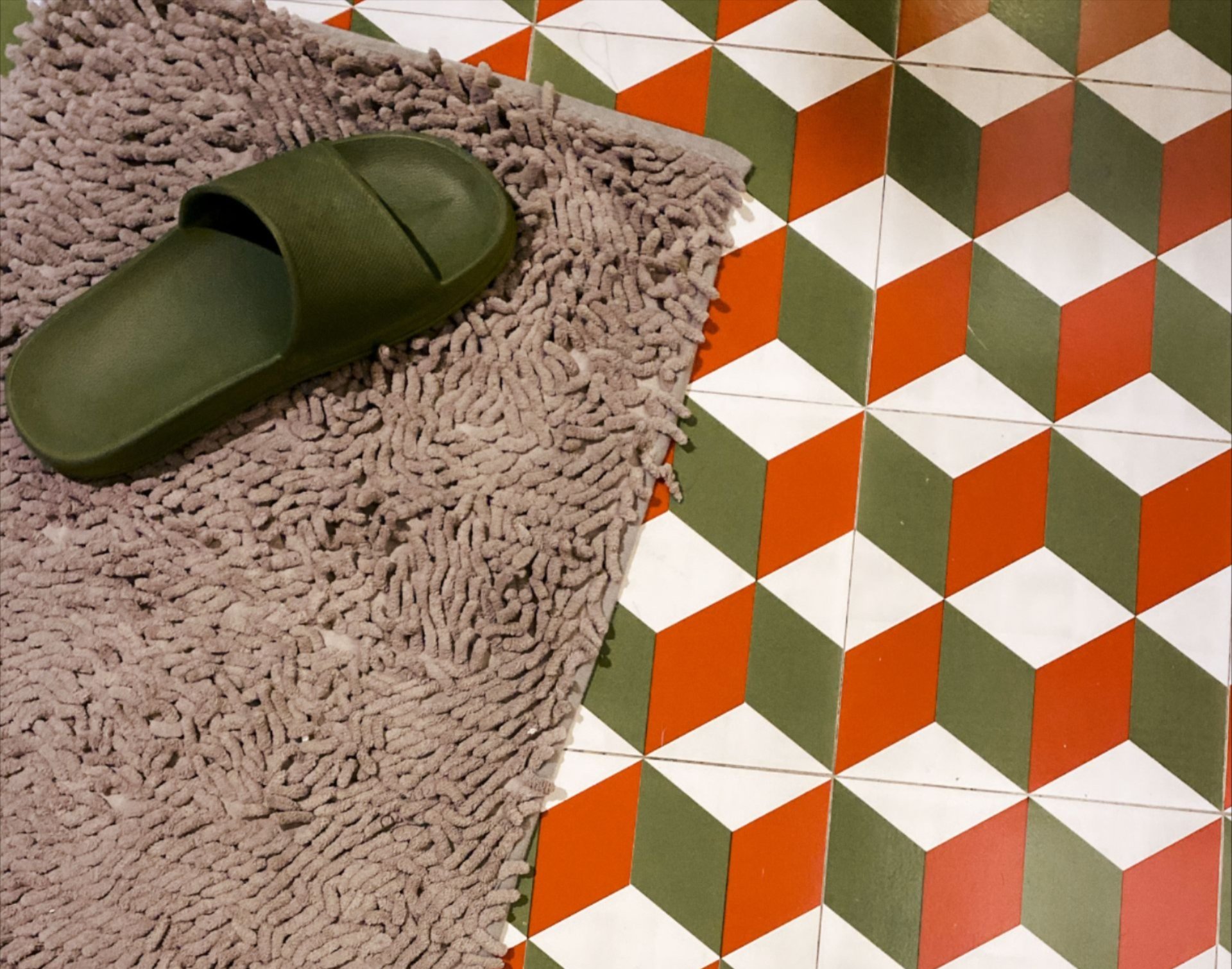 Green slippers on a pink shag bath mat beside a bold orange and green geometric tile floor