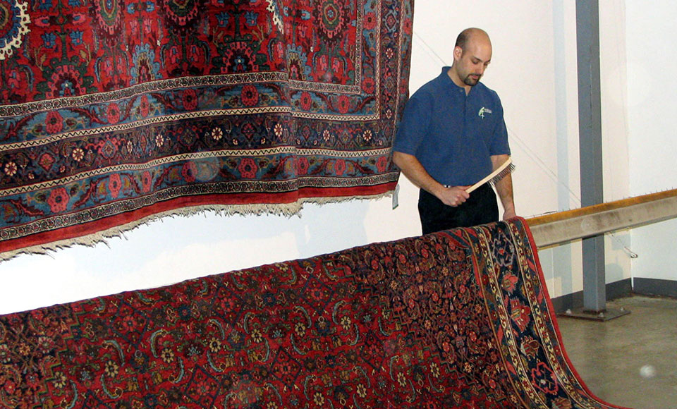Technician hanging a large red oriental rug over a bar in the controlled drying room