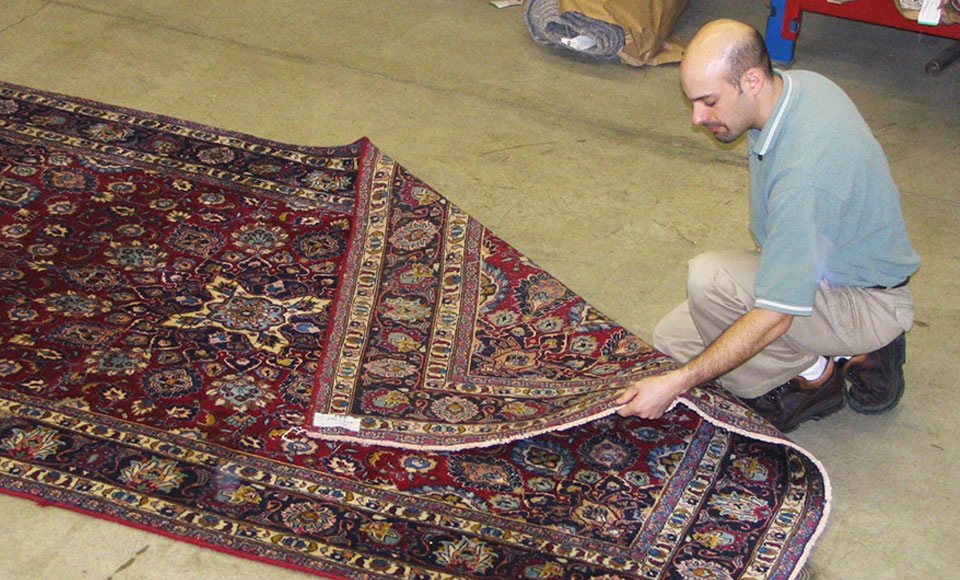 Horrigan technician kneeling to inspect a red patterned oriental rug on the plant floor