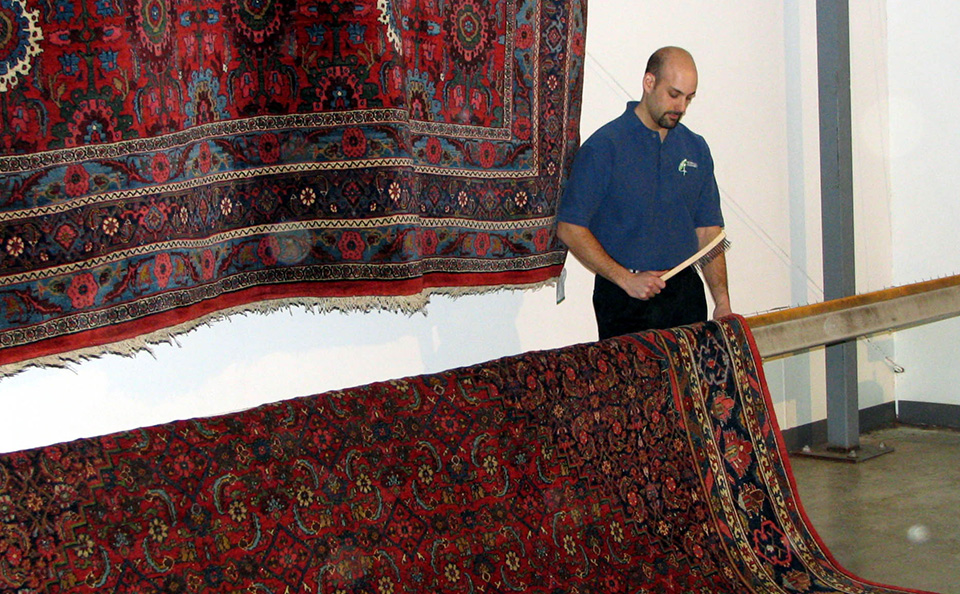 Technician inspecting a large oriental rug hanging in the rug cleaning plant Technician inspecting a large oriental rug hanging in the rug cleaning plant